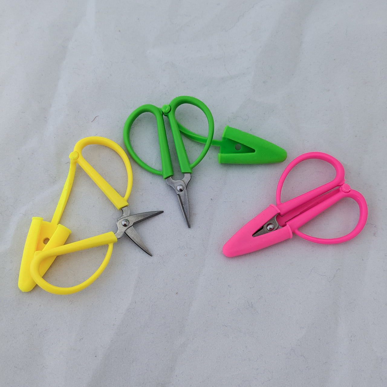 Mini super snips tiny scissors with sleeve shown covered, with the cover off, and open. Colors are neon yellow, green, and pink.